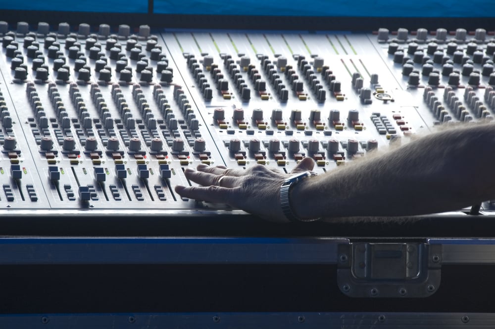 Technicians left hand makes adjustment on audio control panel in booth at outdoor concert